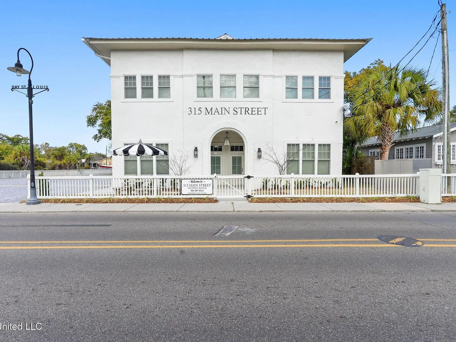 The white stucco front of 315A Main Street with its arched entry, picket fence and black-and-white striped umbrella