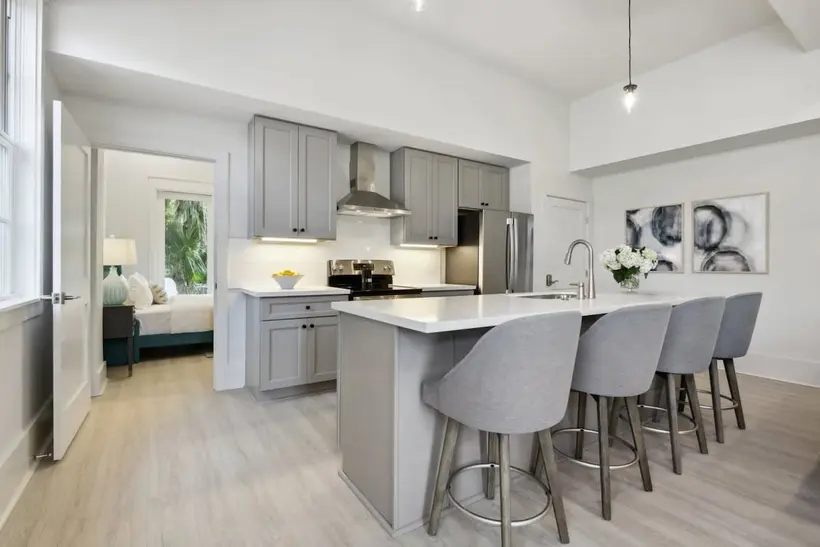 Kitchen with a white quartz island, four gray bar stools, gray cabinets and stainless appliances